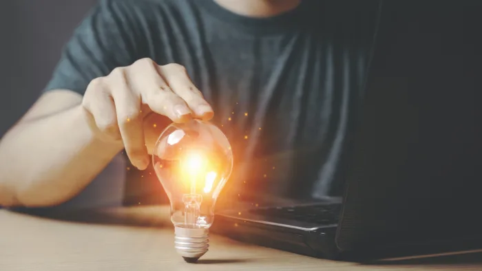 person touching a lightbulb while on their computer