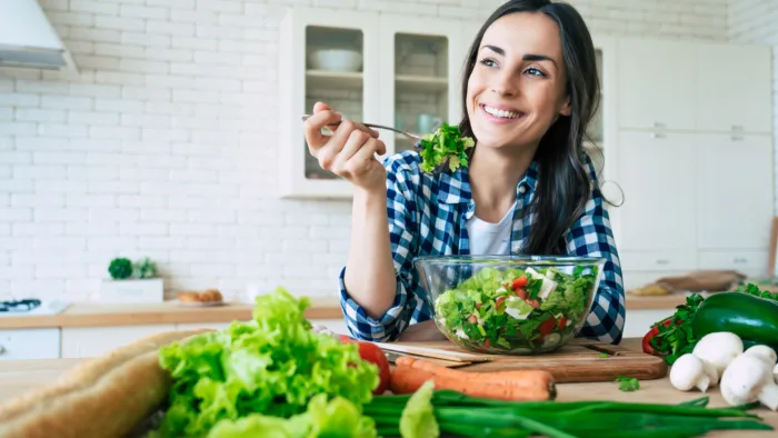 person smiles while eating a fresh salad at the table
